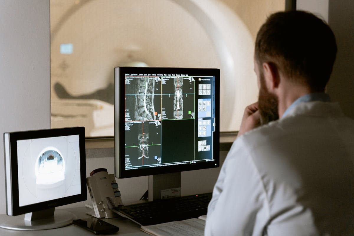 Radiologist reviewing spine MRI scans at workstation with MRI scanner visible